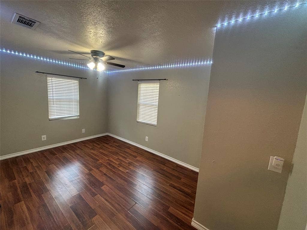 910 NE 31st, Grand Prairie, TX 75050 Spacious room featuring wood-finish flooring, two windows with blinds, a ceiling fan, and crown molding