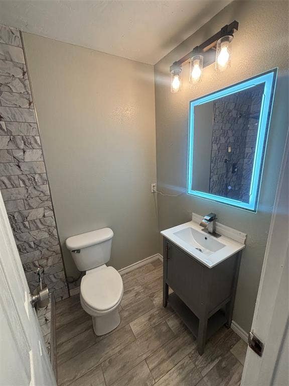 910 NE 31st, Grand Prairie, TX 75050 Bathroom featuring wood-finish flooring, a contemporary vanity with a white countertop and integrated sink, and an illuminated mirror