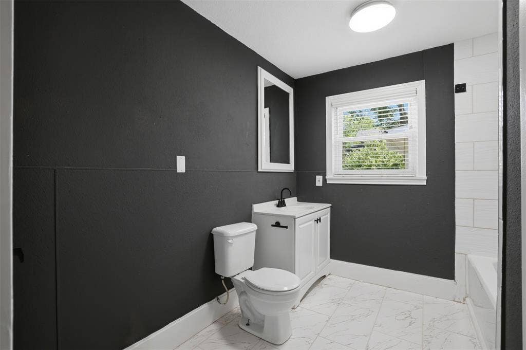 337 N 1st Street, Point, TX 75472 Bathroom featuring dark accent wall, white vanity with matte black hardware, white subway tile shower surround, and a window with blinds