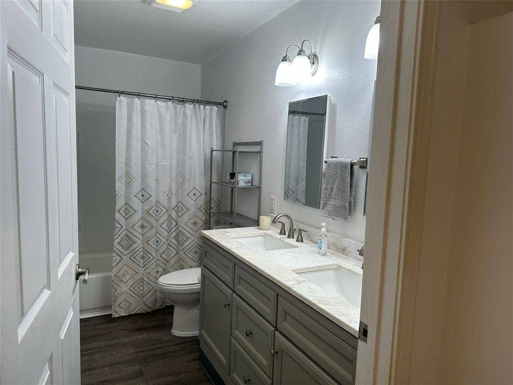144 Huntoon Trail, Mabank, TX 75156 Bathroom featuring a dual vanity with a light-toned countertop, wood-finish flooring, a white porcelain toilet, and a combined tub and shower
