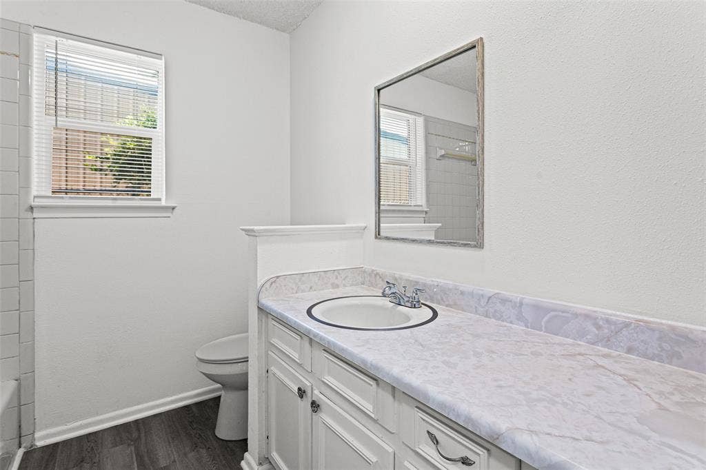 529 Georgetown Drive, Everman, TX 76140 Bathroom featuring a vanity with a white countertop and integrated sink, white cabinetry with dark hardware, a framed mirror, and wood-finish flooring
