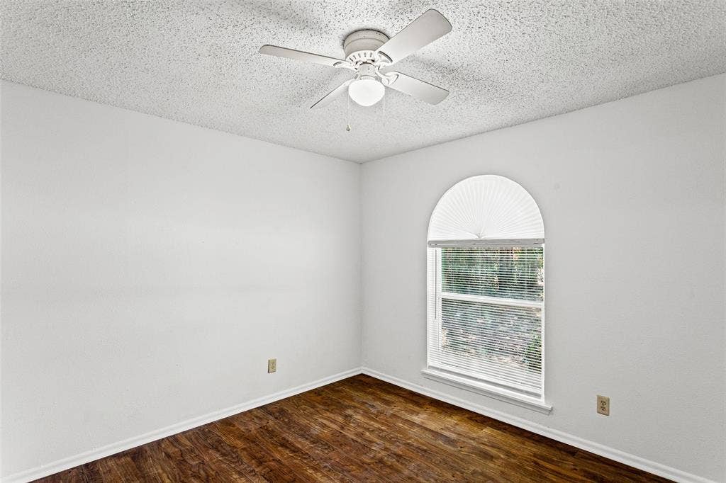 529 Georgetown Drive, Everman, TX 76140 Arched window with pleated shade, wood-finish flooring, white baseboards, and a white ceiling fan with integrated lighting