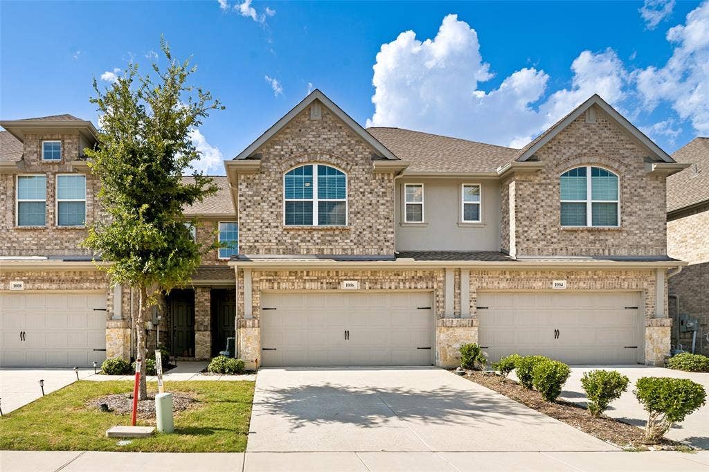 1006 Emil Place, Allen, TX 75013 Brick facade townhouse featuring an attached garage, arched window, and mature landscaping