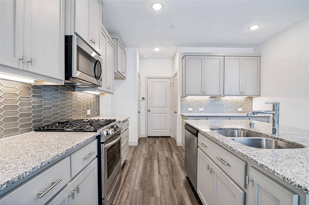 1006 Emil Place, Allen, TX 75013 Modern kitchen featuring light gray cabinetry with brushed nickel hardware, granite countertops, stainless steel appliances, a gray picket tile backsplash, and wood-finish flooring