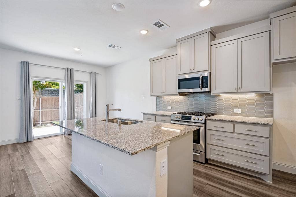 1006 Emil Place, Allen, TX 75013 Modern kitchen featuring an island with a double basin sink, granite countertops, and stainless steel appliances