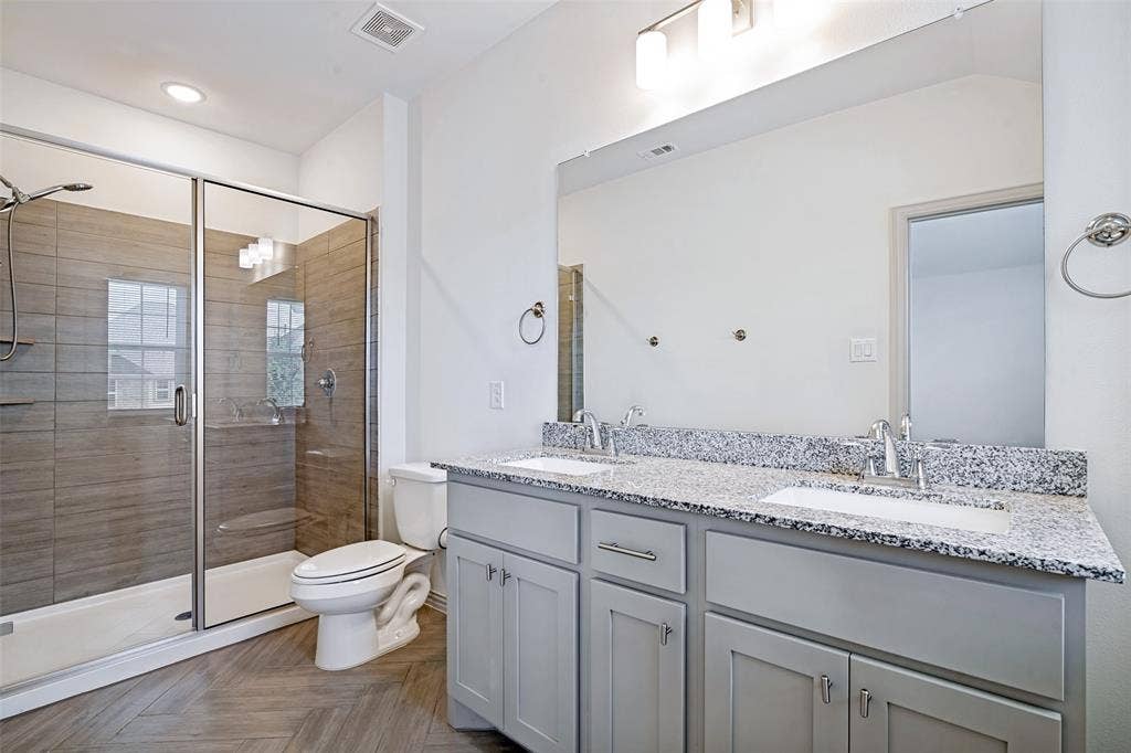 1006 Emil Place, Allen, TX 75013 Contemporary bathroom featuring a spacious glass-enclosed shower with horizontal tile work, a dual vanity with light gray cabinetry, and a speckled countertop
