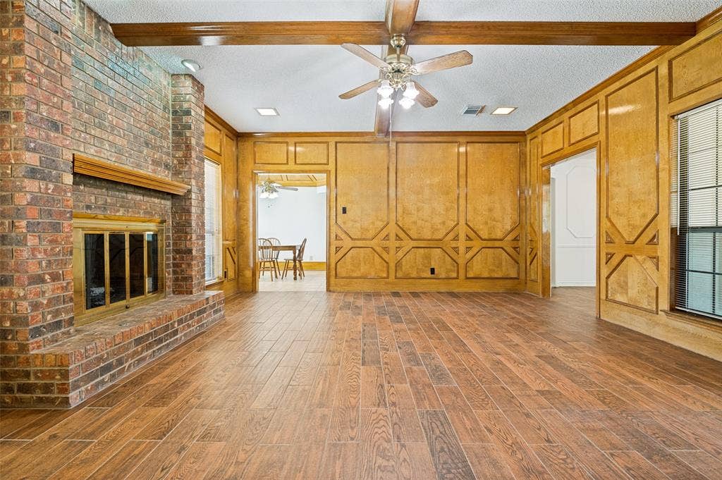 131 Honey Tree Lane, DeSoto, TX 75115 Spacious living area featuring wood-finish flooring, a brick fireplace with a mantel, and decorative wood paneling