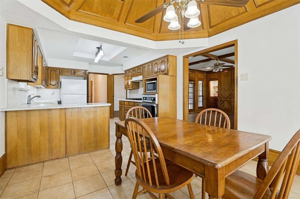 131 Honey Tree Lane, DeSoto, TX 75115 Kitchen featuring wood-finish cabinetry, tile flooring, recessed ceiling with wood-finish paneling, and an integrated counter bar
