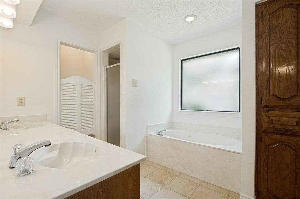 131 Honey Tree Lane, DeSoto, TX 75115 Bathroom featuring a dual vanity with shell-shaped sinks, a built-in soaking tub, a frosted window, and wood cabinetry