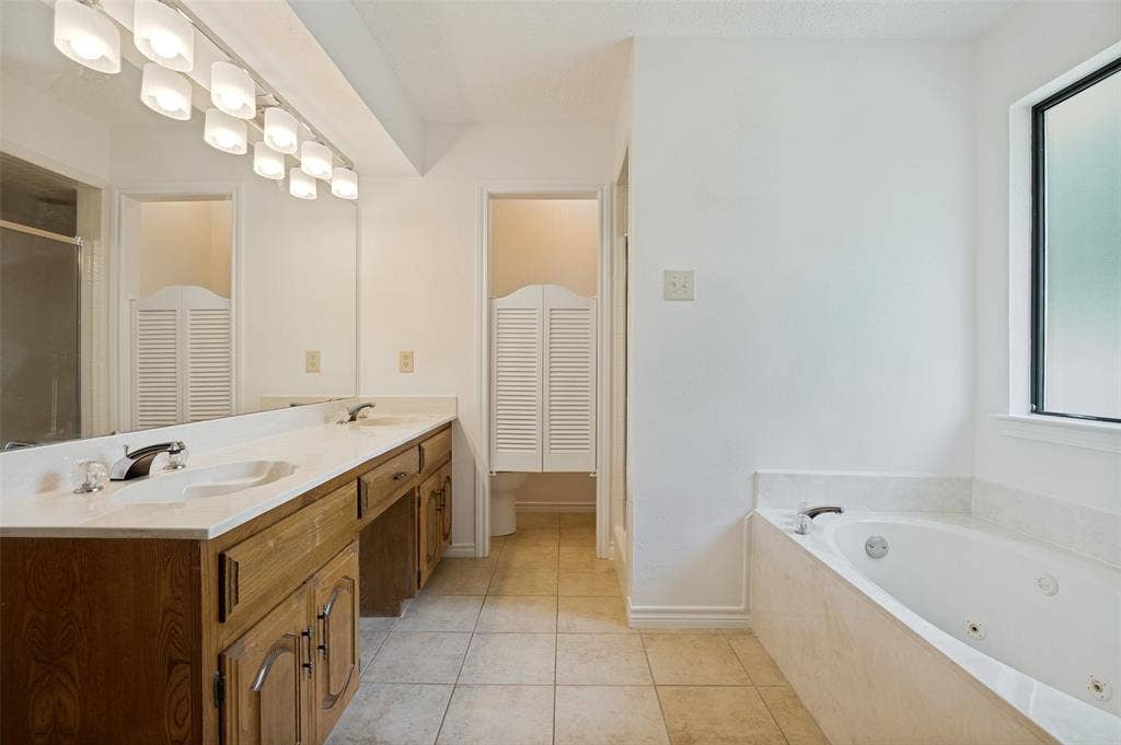 131 Honey Tree Lane, DeSoto, TX 75115 Bathroom featuring a dual vanity with wood cabinetry, a built-in jetted tub, tiled flooring, and a privacy window