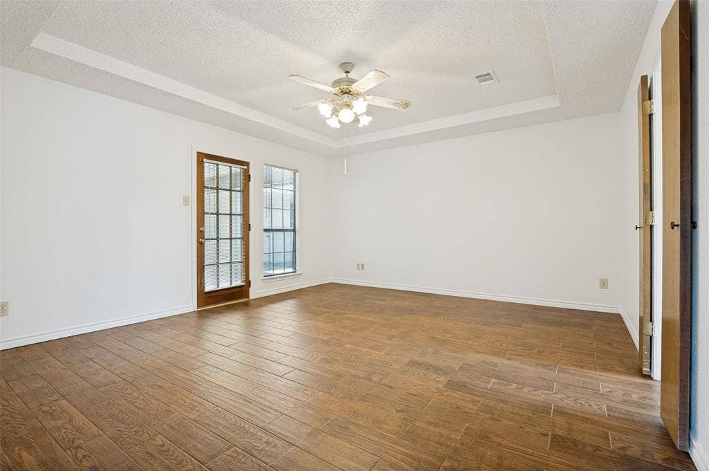 131 Honey Tree Lane, DeSoto, TX 75115 Spacious room featuring rich wood-finish flooring, a tray ceiling, and a ceiling fan with integrated lighting
