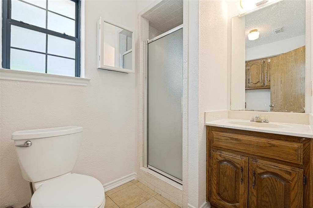 131 Honey Tree Lane, DeSoto, TX 75115 Bathroom with a single-pane window, white toilet, glass-enclosed shower, wood-finish vanity, and integrated sink