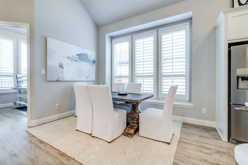 Dining space featuring vaulted ceilings, wood-finish flooring, and a bank of three windows with plantation shutters