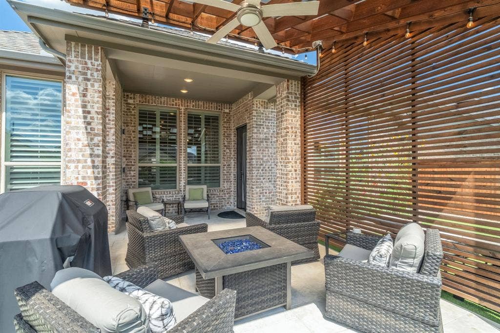 Covered outdoor patio featuring a wood pergola with ceiling fan and string lighting, brick exterior, slatted wood privacy wall, and concrete flooring