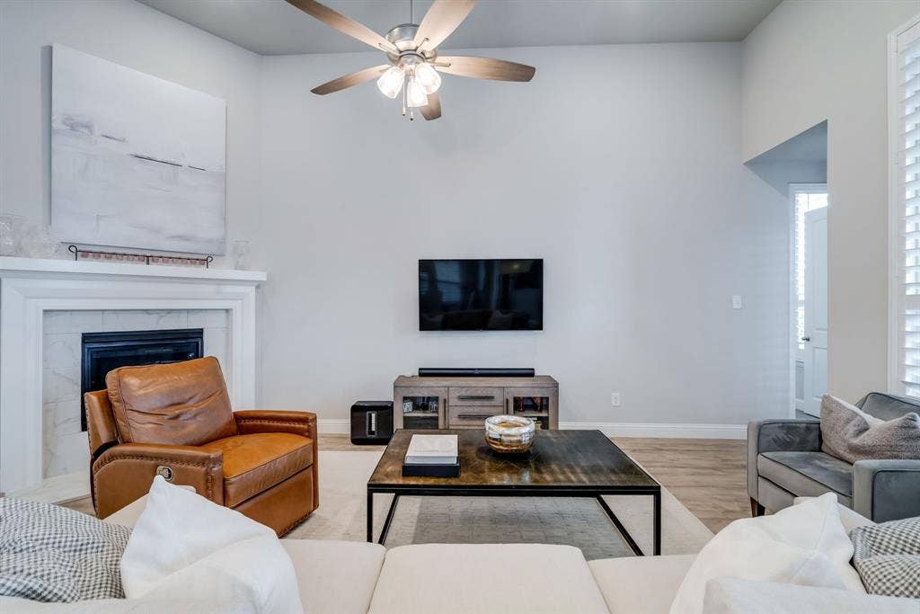 Living space featuring a white mantel fireplace with a black insert, high ceilings, a ceiling fan with light, wood-finish flooring, and white plantation shutters