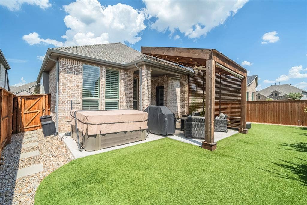 Expansive backyard featuring a stone patio, a wooden pergola, artificial turf, a gravel pathway with stepping stones, and a privacy fence