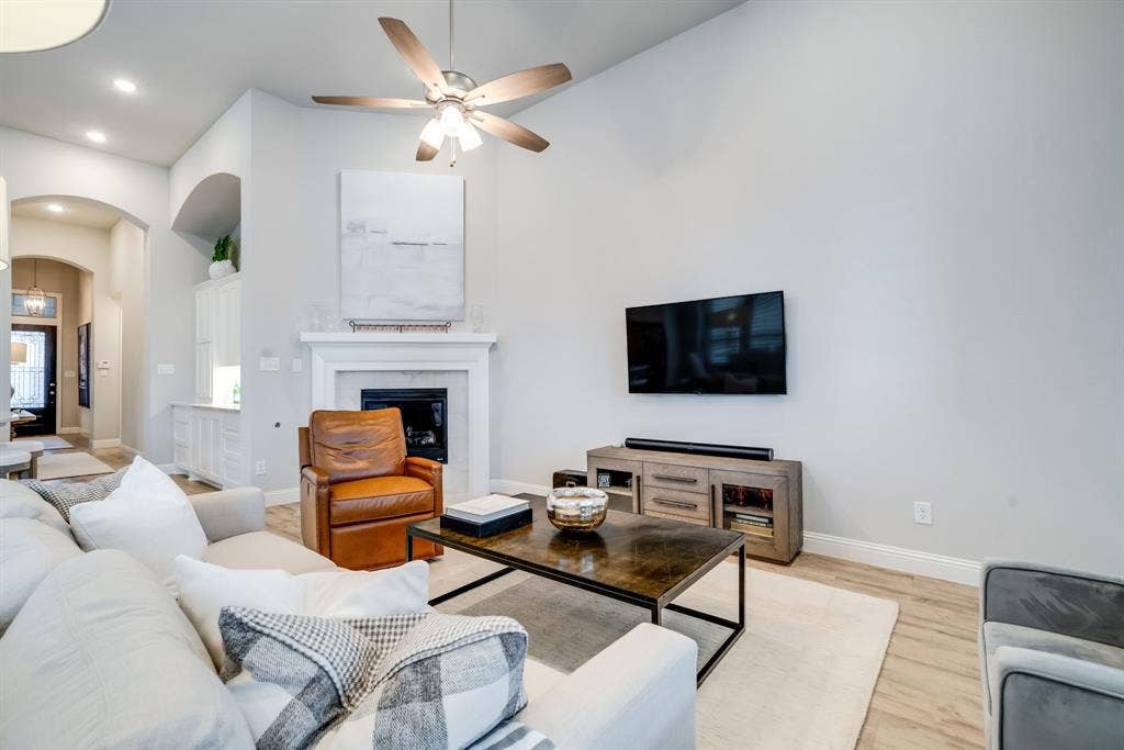 Living area featuring a fireplace with a white mantel, high ceilings, wood-finish flooring, a ceiling fan, and recessed lighting