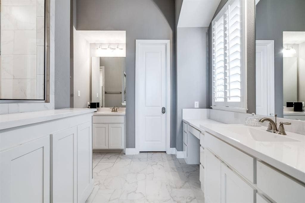 Spacious bathroom featuring a glass-enclosed shower, dual white vanities with integrated sinks, and matching white cabinetry