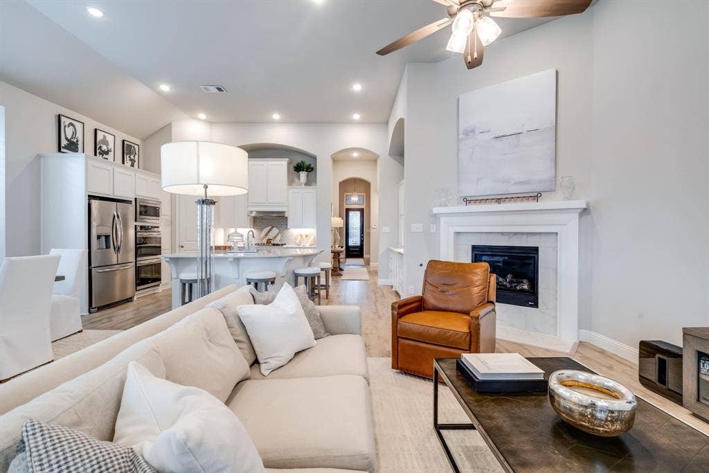 Open-concept living area featuring wood-finish flooring, a contemporary fireplace with a white mantel, and recessed lighting
