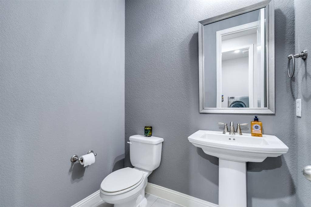 Compact bath featuring a pedestal sink with a chrome faucet, a white toilet, and a framed mirror
