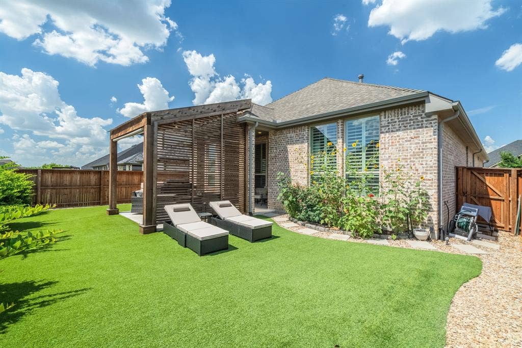 Landscaped backyard featuring a slatted wood pergola, brick exterior, and artificial turf
