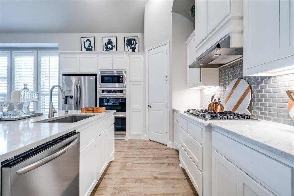 Kitchen featuring white cabinetry, light-toned countertops, stainless steel appliances, a center island with an integrated sink, and wood-finish flooring