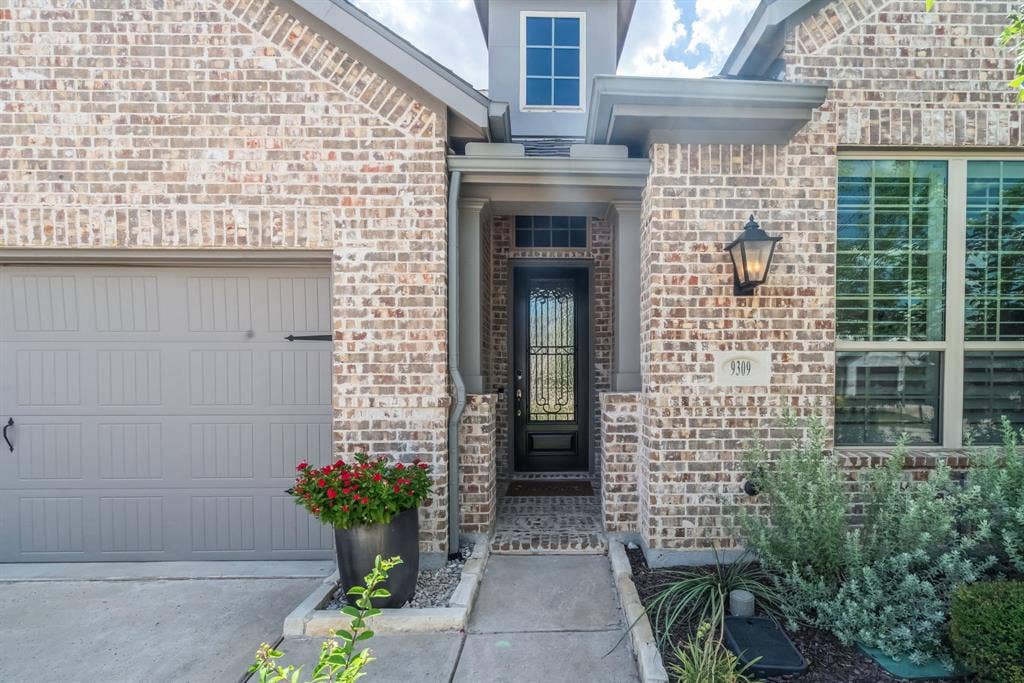 Brick facade featuring a covered entryway with a decorative glass door, a paneled garage door, and a prominent exterior lantern fixture