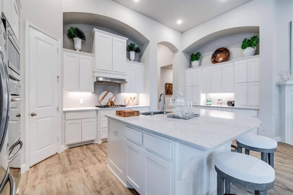 Kitchen featuring white cabinetry, light countertops, wood-finish flooring, stainless steel appliances, and a tiled backsplash