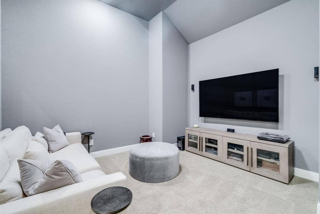 Carpeted room featuring a media console with glass-front cabinetry, wall-mounted speakers, and an accent wall with a varied ceiling height