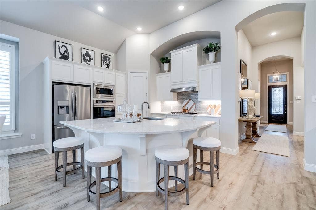 Kitchen featuring a curved central island with white countertop, white cabinetry, stainless steel appliances, and light wood-finish flooring