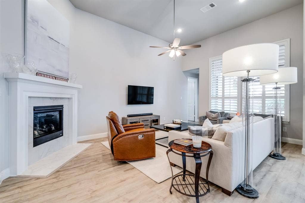 Spacious living area featuring high vaulted ceilings, light wood-finish flooring, and a fireplace with a white mantel and light-toned tile surround