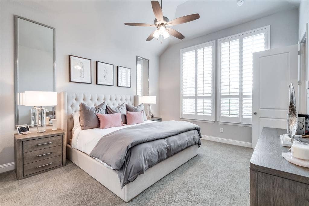 Spacious bedroom featuring plush carpeting, a vaulted ceiling, and two tall windows with plantation shutters