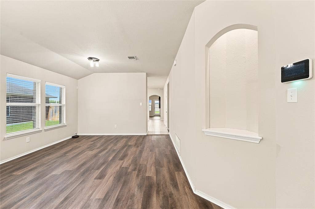 Spacious room featuring wood-finish flooring, light-colored walls, and multiple windows with blinds