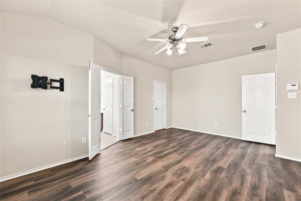 Spacious room featuring wood-finish flooring, light-toned walls, and a ceiling fan with integrated lighting