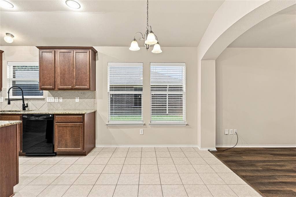 Kitchen and dining area featuring wood cabinetry, black appliances, tile flooring, and an arched entryway