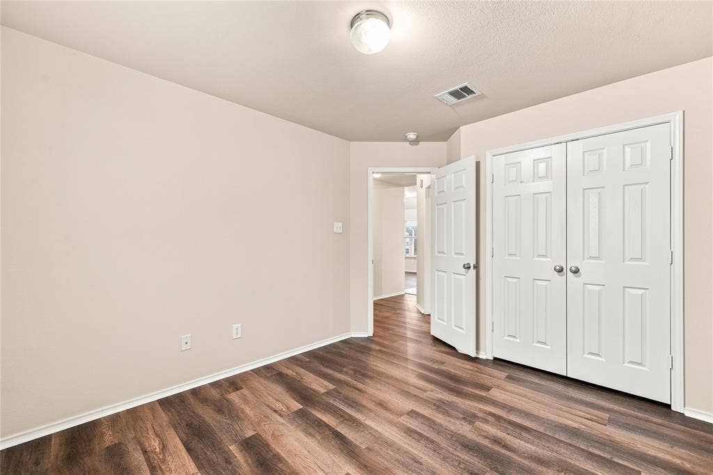 Room featuring wood-finish flooring, light-toned walls, white baseboards, and a ceiling-mounted light fixture