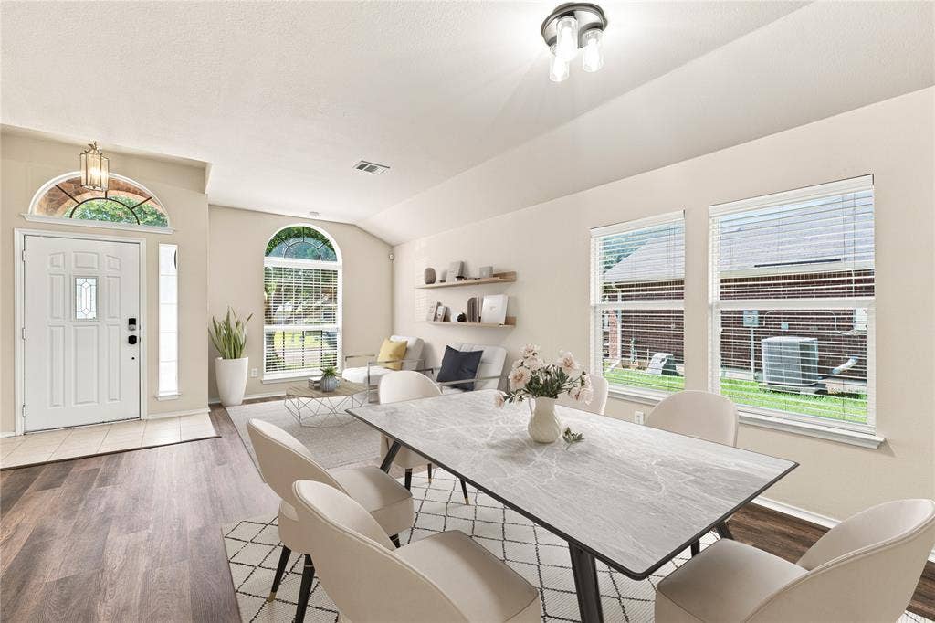 Combined dining and living area featuring wood-finish flooring, vaulted ceilings, and a light color palette