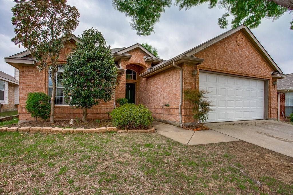 9213 Norfolk Lane, McKinney, TX 75071 Brick facade residence featuring an arched entry, an attached garage, a paved driveway, and mature landscaping