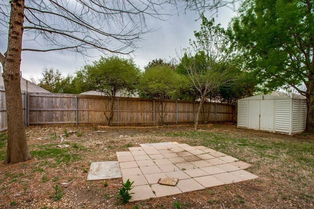 9213 Norfolk Lane, McKinney, TX 75071 Spacious backyard featuring a wood privacy fence, established trees, a paver patio area, and a white storage shed