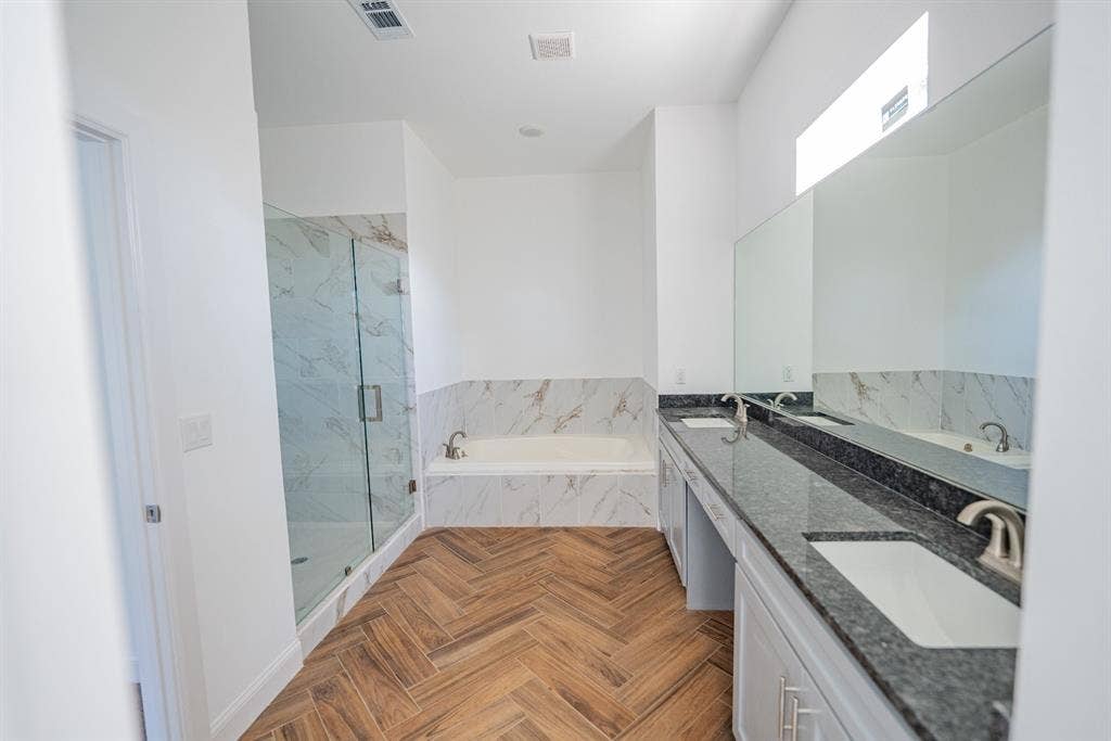 1408 Spinnaker Lane, Azle, TX 76020 Spacious bathroom featuring a dual vanity with dark stone countertops, wood-finish herringbone flooring, a deep soaking tub, a glass-enclosed shower, and a high transom window