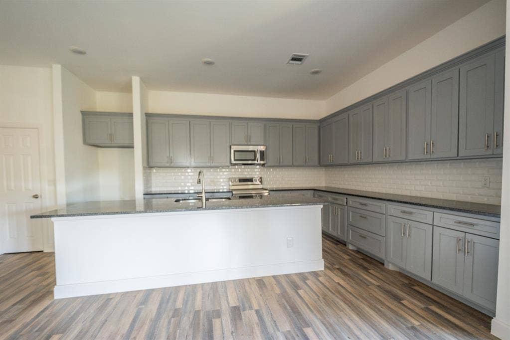 1408 Spinnaker Lane, Azle, TX 76020 Kitchen featuring gray shaker-style cabinetry, a built-in microwave, stainless steel range, white subway tile backsplash, and wood-finish flooring