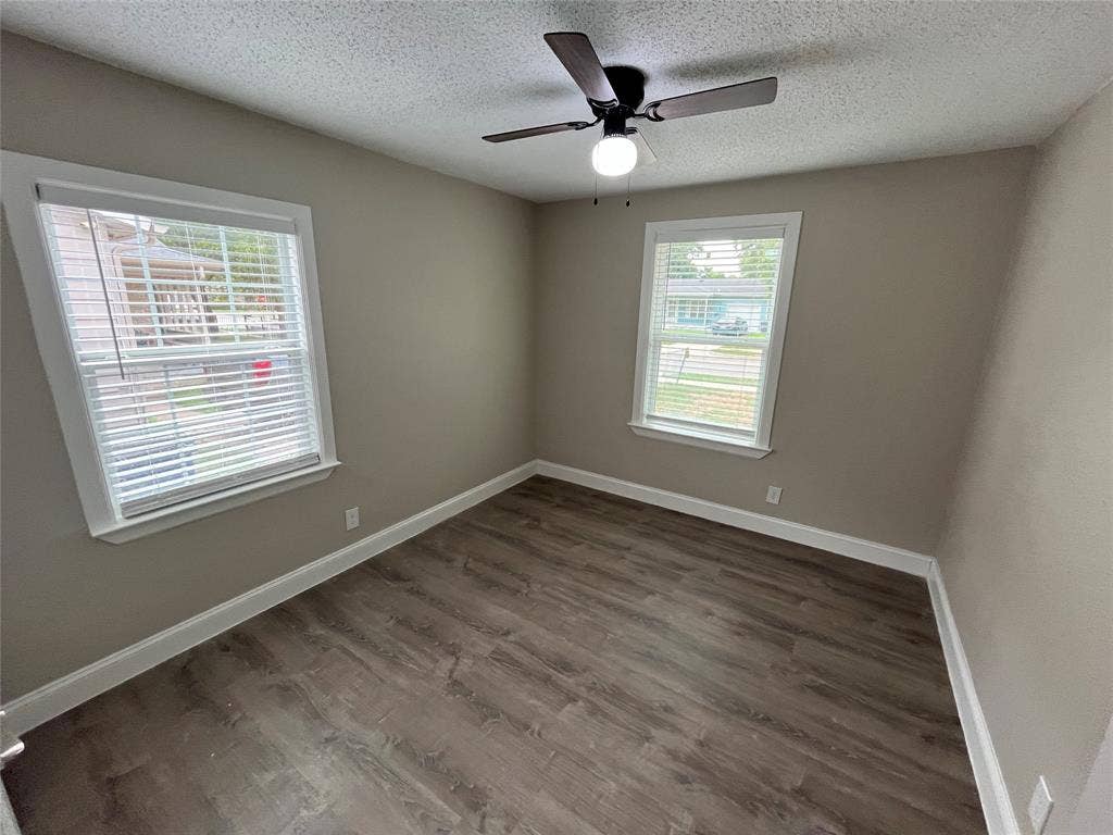 719 Fairwood Drive, Dallas, TX 75232 Room featuring wood-finish flooring, two windows with white blinds, and a dark-toned ceiling fan with an integrated light fixture