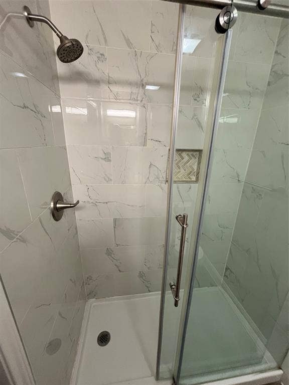 719 Fairwood Drive, Dallas, TX 75232 Shower enclosure featuring white marble-look subway tile, a recessed niche with herringbone pattern accent tile, a sliding glass door, a white shower pan, and brushed nickel fixtures