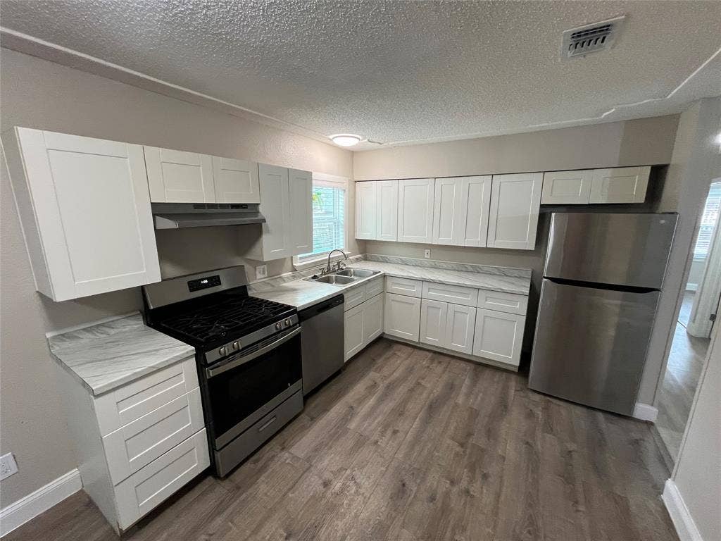 719 Fairwood Drive, Dallas, TX 75232 Modern kitchen featuring a gas range, stainless steel appliances, white shaker cabinetry, wood-finish flooring, and light-toned countertops
