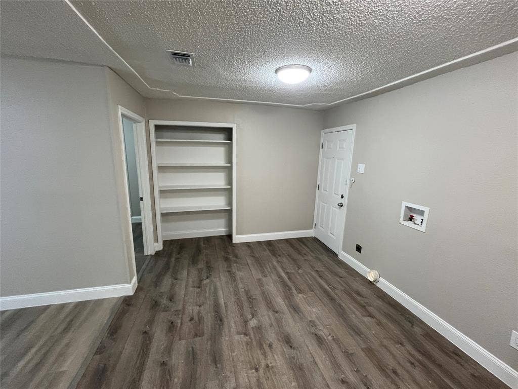 719 Fairwood Drive, Dallas, TX 75232 Room featuring neutral wall paint, wood-finish flooring, built-in shelving, a paneled door, and a utility hookup