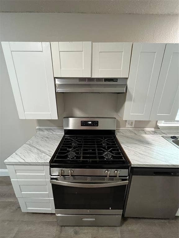 719 Fairwood Drive, Dallas, TX 75232 Stainless steel range with a gas cooktop, under-cabinet range hood, white shaker-style cabinetry, white countertops with gray veining, and wood-finish flooring