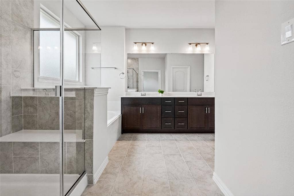 10008 Birchpoint Drive, Fort Worth, TX 76108 Tiled flooring throughout, glass-enclosed shower with a built-in bench, double vanity with dark wood-finish cabinetry, integrated dual sinks, and two large mirrors