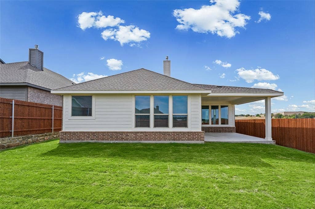 10008 Birchpoint Drive, Fort Worth, TX 76108 Expansive backyard featuring a manicured lawn, a covered concrete patio, wood fencing, and a stone retaining wall
