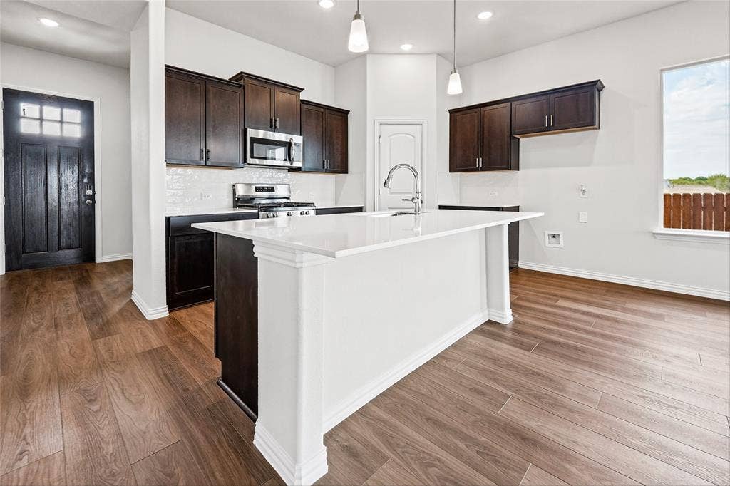 10008 Birchpoint Drive, Fort Worth, TX 76108 Kitchen island with white countertop, dark wood-finish cabinetry, stainless steel appliances, and wood-finish flooring