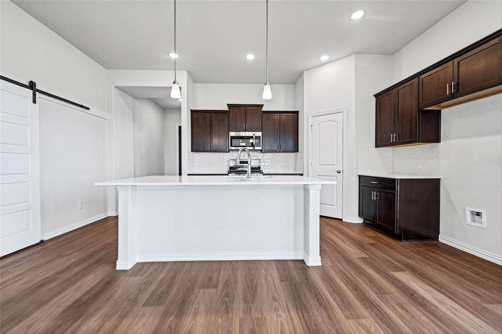10008 Birchpoint Drive, Fort Worth, TX 76108 Kitchen featuring wood-finish flooring, dark wood cabinetry, white subway tile backsplash, white countertops, and a kitchen island with pendant lighting